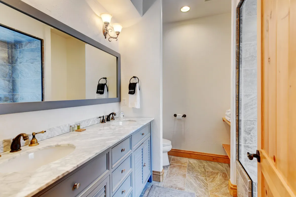 A sophisticated bathroom with a marble countertop, a large mirror above the sink, and elegant bronze fixtures. Soft lighting and wooden accents create a serene, spa-like atmosphere, perfect for unwinding after a busy day.