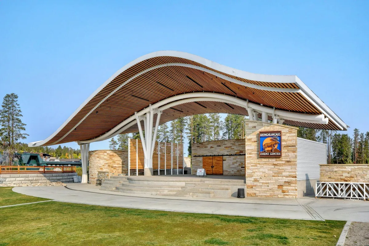 This image captures the vibrant exterior of the Hideaway Park Amphitheater, featuring its distinctive curvilinear roof, a welcoming stone facade, and signage indicating ongoing community events. The scene is lively, hinting at concerts, art fairs, and local gatherings that make the downtown Winter Park experience special.