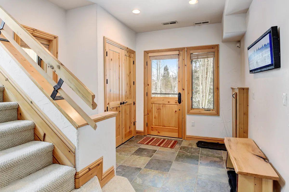A cozy and inviting entryway featuring a staircase, front door, stone flooring, and a wooden bench. The area is perfectly suited for putting on or taking off shoes, organizing outdoor gear, or pausing before heading out.