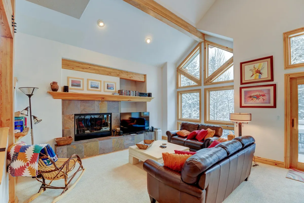 A welcoming living area featuring large windows that offer sweeping views, a cozy fireplace, comfortable seating adorned with decorative pillows, and a serene, light-filled ambiance ideal for both relaxation and work.