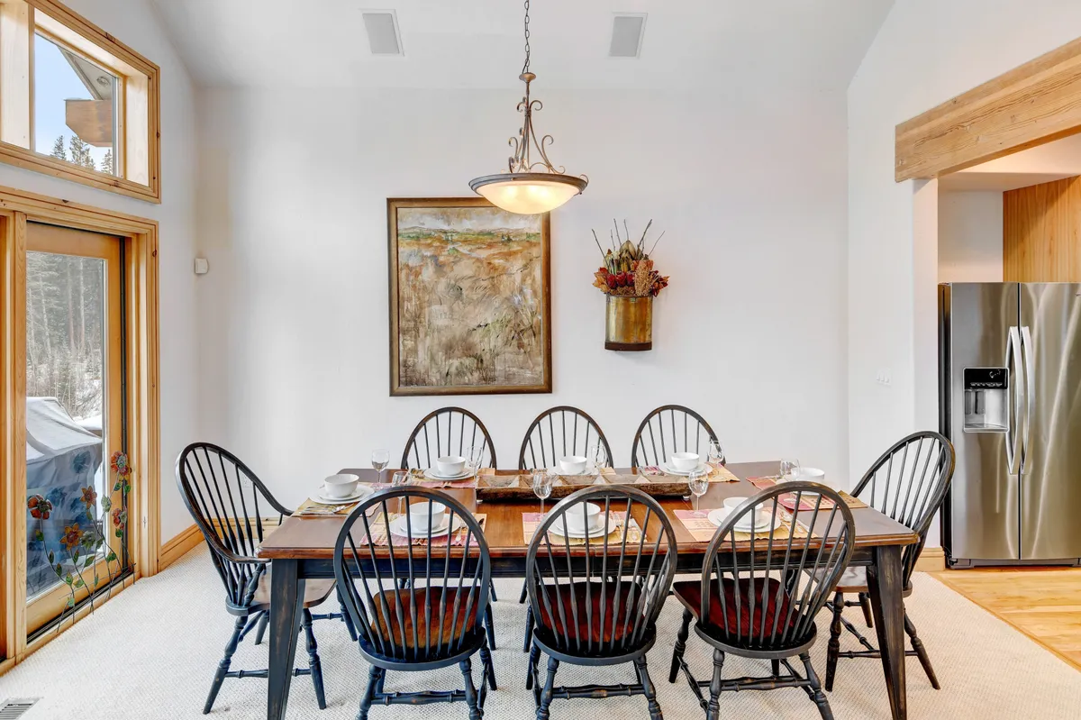 A dining area with a prominent chandelier, an elegant table set for a meal, and artwork adorning the walls. Natural light floods the space through large windows, creating a warm ambiance ideal for family dinners and intimate celebrations.
