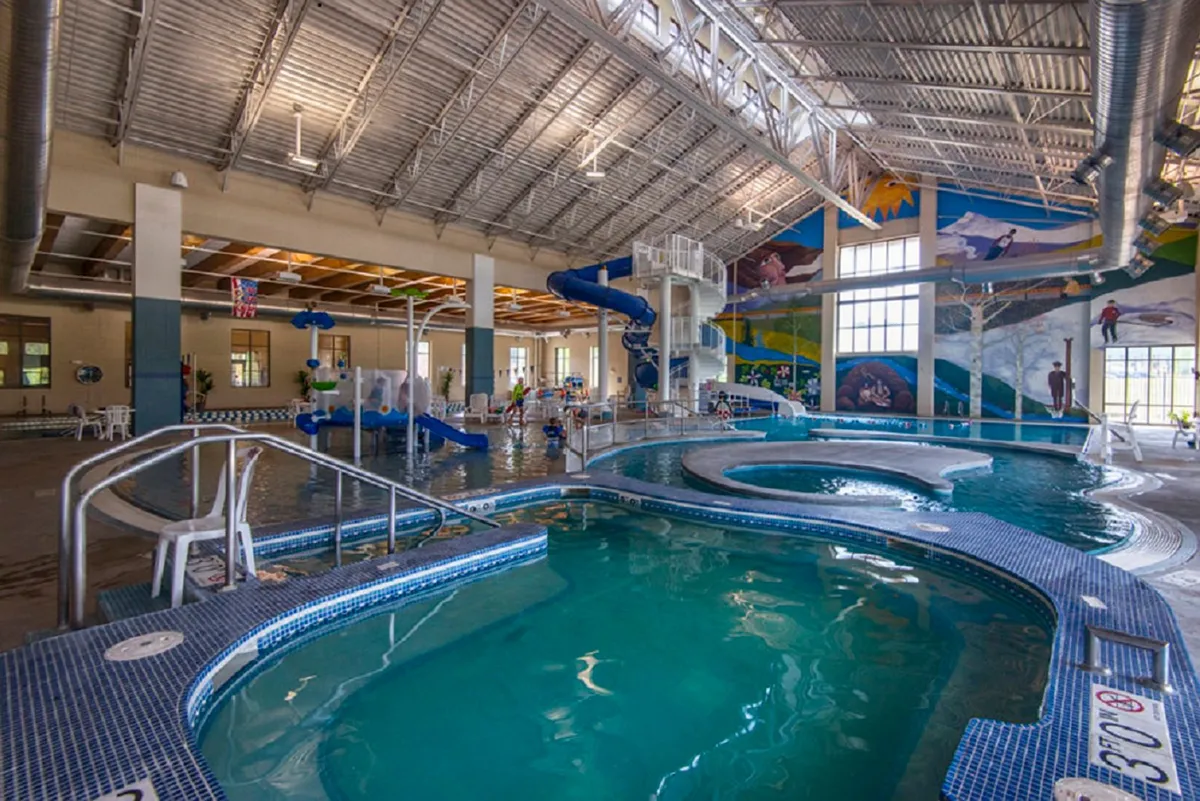 A vibrant indoor pool area complete with water slides, a mural, children playing, and lounge chairs. The space is lively and family-friendly, capturing the joy of group activities and kid-centered amenities.
