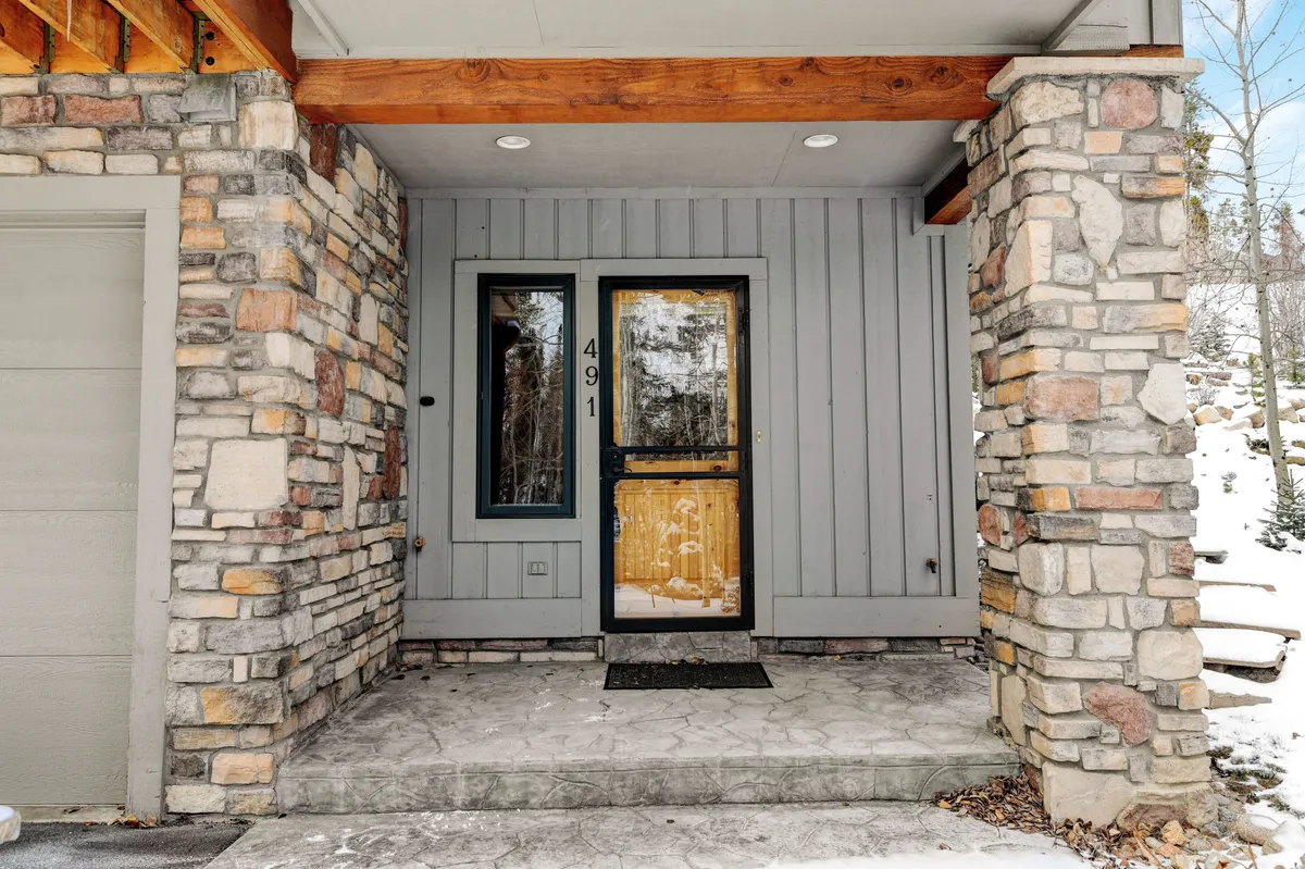 A warm and welcoming exterior view of the villa's front entrance, featuring stone pillars, a concrete porch, and a tastefully decorated front door. The scene suggests a cozy and inviting home base for all the nearby adventures.