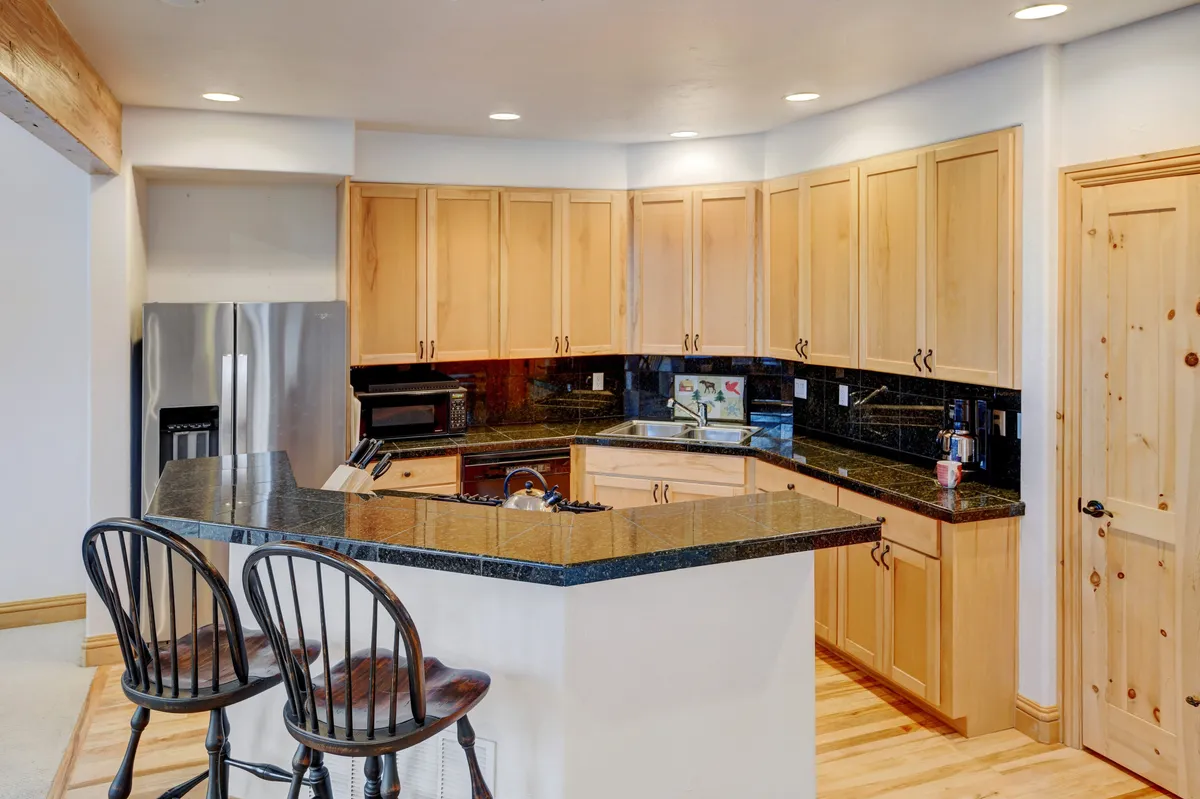 A bright and modern kitchen with a spacious island, comfortable bar stools, and sleek cabinetry. The open layout allows for interaction between the kitchen, breakfast bar, and adjacent living spaces.