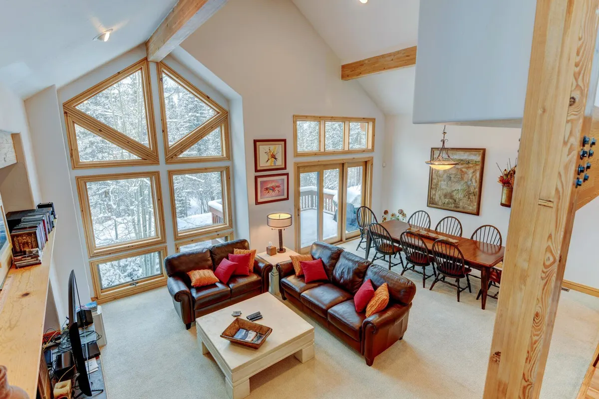 A spacious, inviting open-plan area featuring a large dining table and a comfortable seating area, framed by expansive windows that offer views of the snowy outdoors. The scene is set for group meals, games, or relaxed gatherings, with plenty of room for everyone to come together.