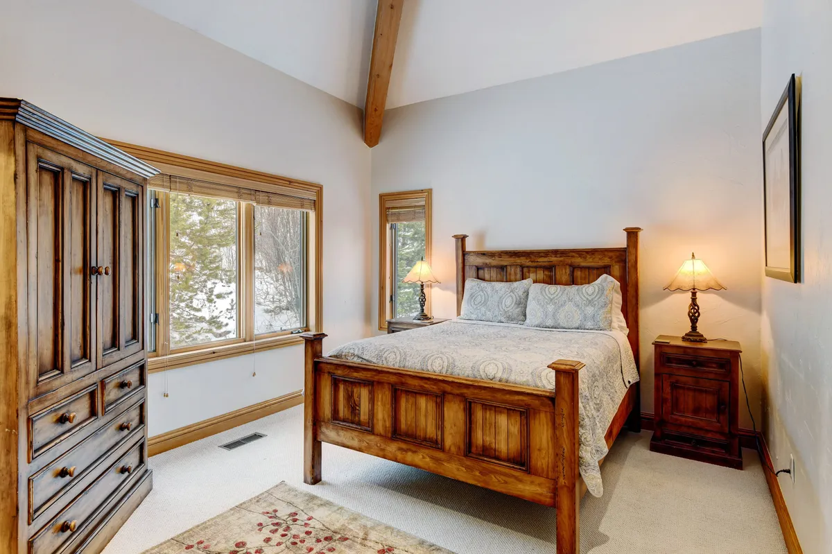 A serene bedroom with a wooden bed frame, soft premium bedding, a side table with a lamp for nighttime reading, a wardrobe for storage, and large windows that allow natural light to stream in. The space exudes comfort and relaxation, ideal for restful nights.