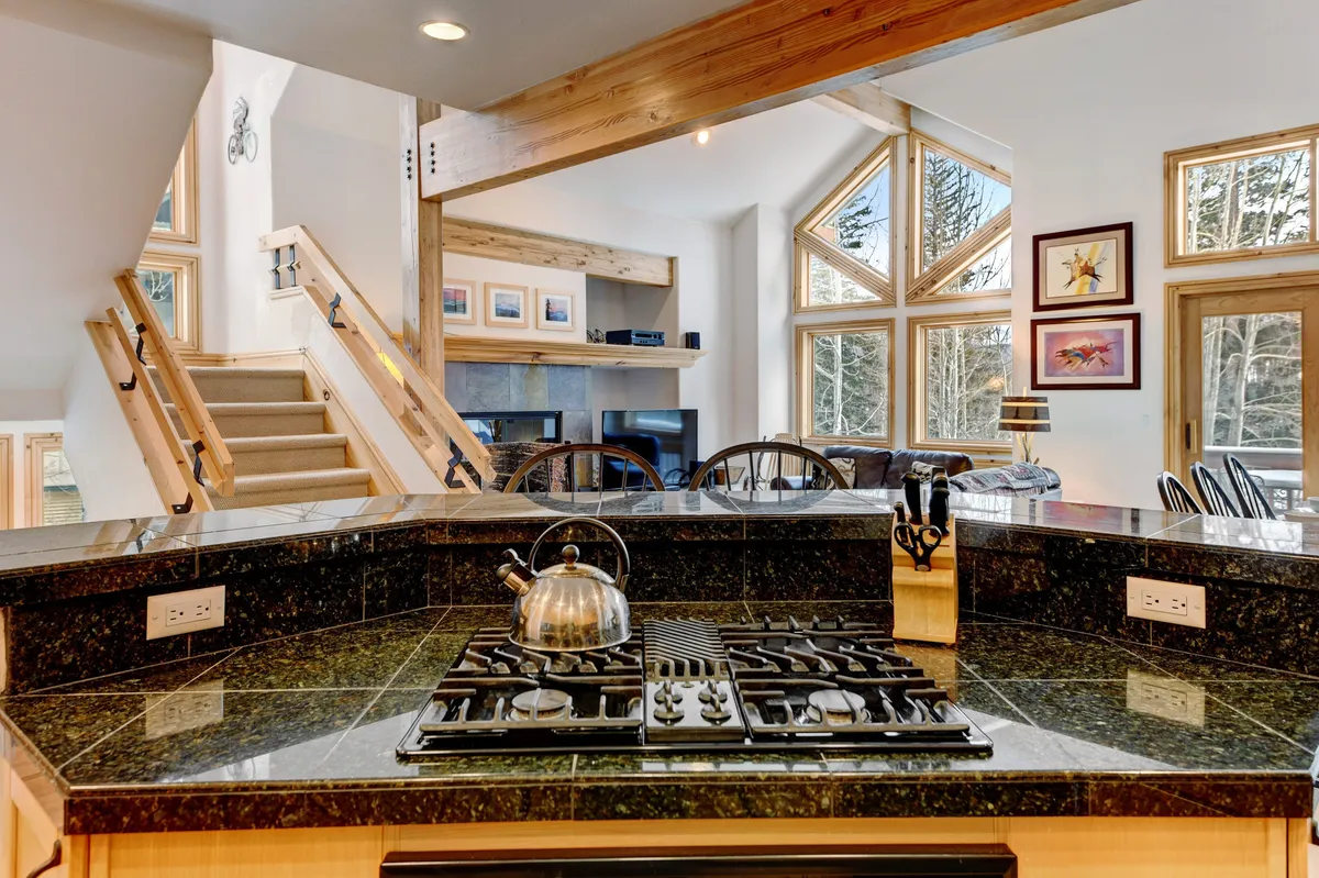 An inviting kitchen and dining space with a kitchen island, stainless steel kettle, large windows, and a staircase, suggesting a seamless flow between indoor comfort and the outdoors.