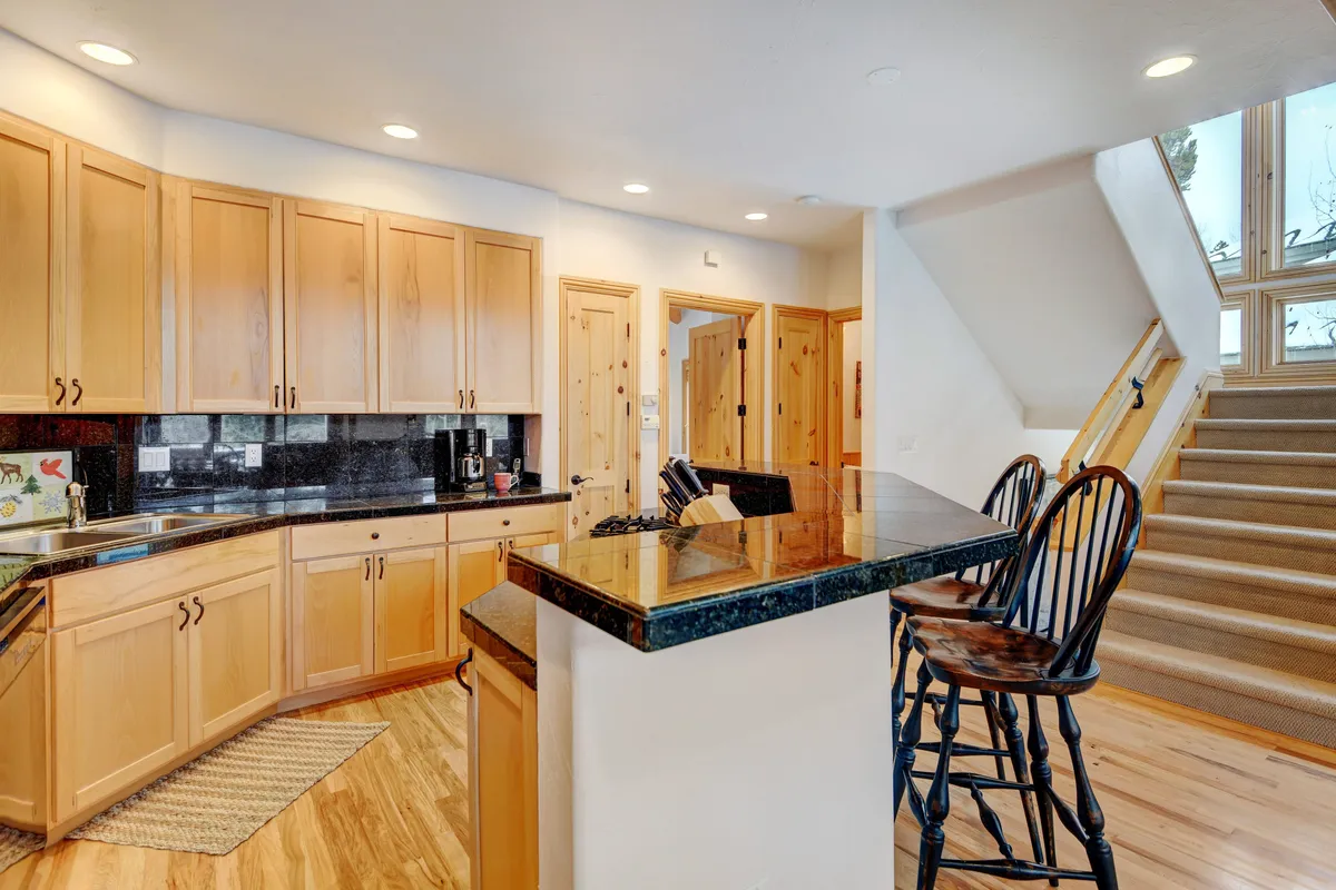 This image features a sleek, modern kitchen with a prominent kitchen island, bar stools, stainless steel appliances, black countertops, and ample cabinetry. The setup is open and inviting, perfect for families or groups to gather, cook, and socialize.