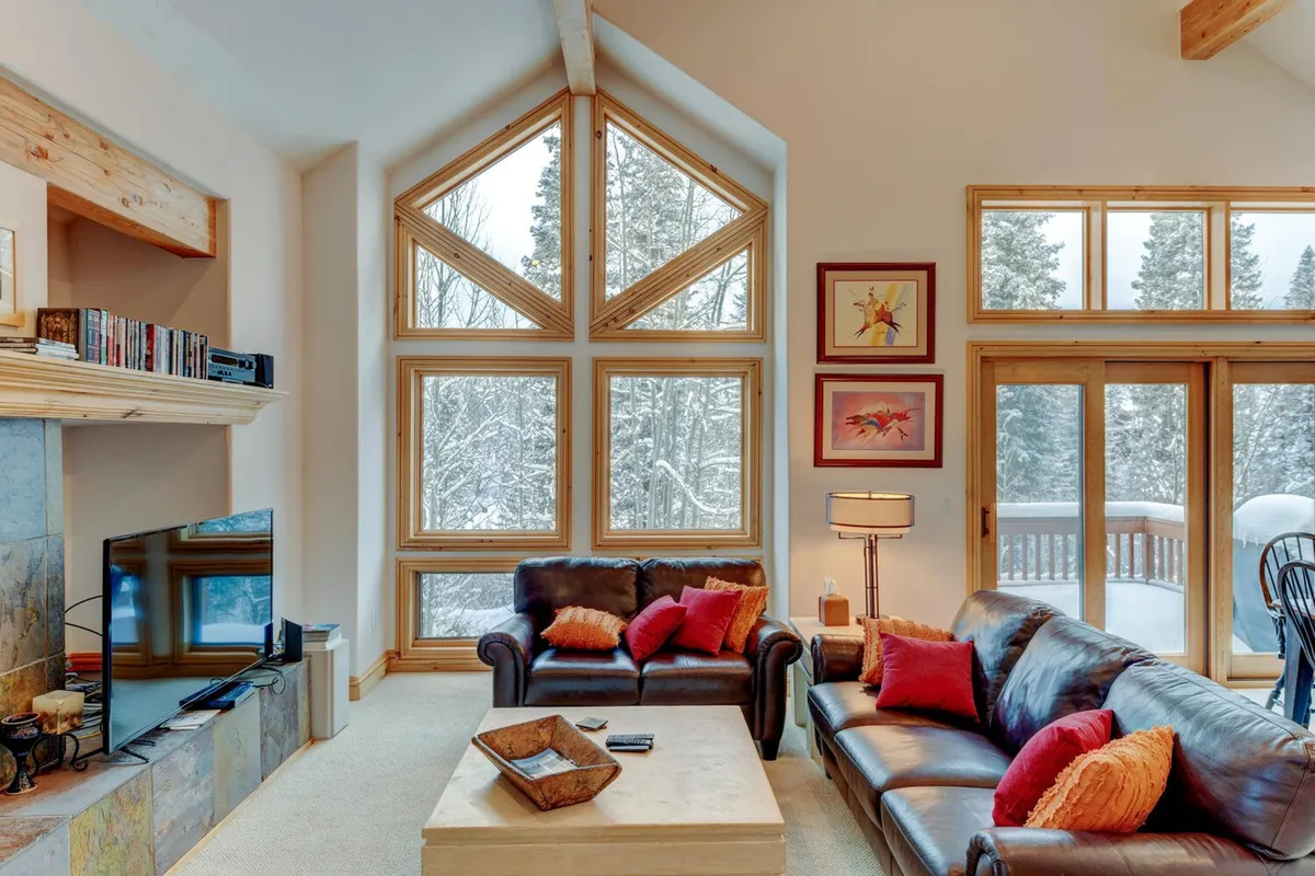 A living area featuring plush leather sofas arranged around a coffee table and a welcoming fireplace, all bathed in natural light from large windows. The scene invites guests to relax together, watch TV, or enjoy a warm drink while engaging in lively conversation.