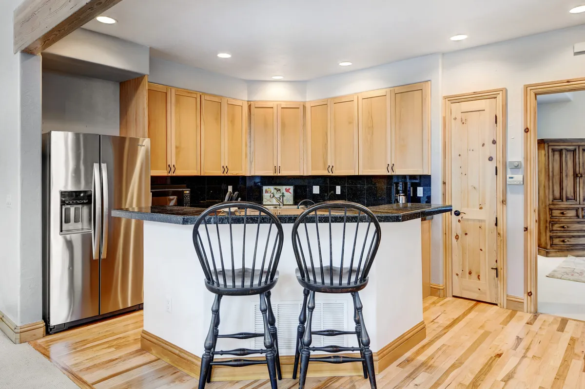 A cozy kitchen scene with a kitchen island, bar stools, and a stainless steel refrigerator. The space feels warm and homey, ideal for group cooking or family meals, with features that invite participation from all ages.